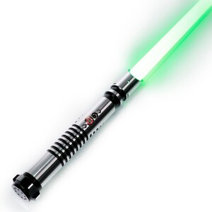 K&ouml;nnte beinhalten: Ein silbernes und schwarzes Lichtschwert mit einer gr&uuml;nen Klinge. Das Lichtschwert hat einen schwarzen Griff mit einem silbernen Griff und einen roten Knopf.