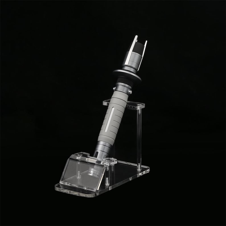 Peut inclure: Une r&eacute;plique de sabre laser argent&eacute;e avec une poign&eacute;e grise et un support en acrylique transparent. Le sabre laser est sur un fond noir.