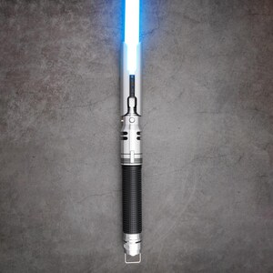 May include: A silver lightsaber with a blue blade. The lightsaber has a black handle with a textured grip.