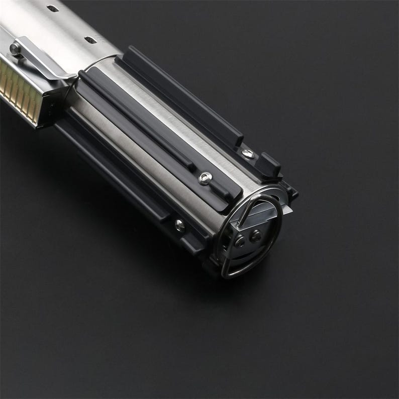 May include: A silver lightsaber hilt with black accents and a metal ring. The hilt has a textured surface and a series of small screws.