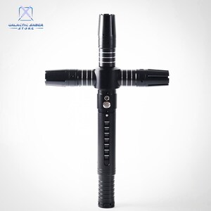 Puede incluir: Un sable de luz negro con guarda cruzada y detalles plateados. El mango presenta l&iacute;neas verticales y un bot&oacute;n. El logotipo de Galactic Saber Store est&aacute; en la esquina superior izquierda. El sable de luz tiene cuatro hojas.