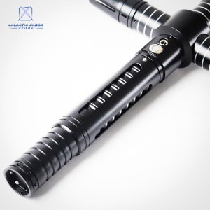 Puede incluir: Un sable de luz negro con un dise&ntilde;o de guarda cruzada. El mango presenta una serie de ranuras y un bot&oacute;n. El sable de luz tiene detalles plateados y est&aacute; sobre un fondo blanco. El logotipo de Galactic Saber Store est&aacute; en la esquina superior izquierda.