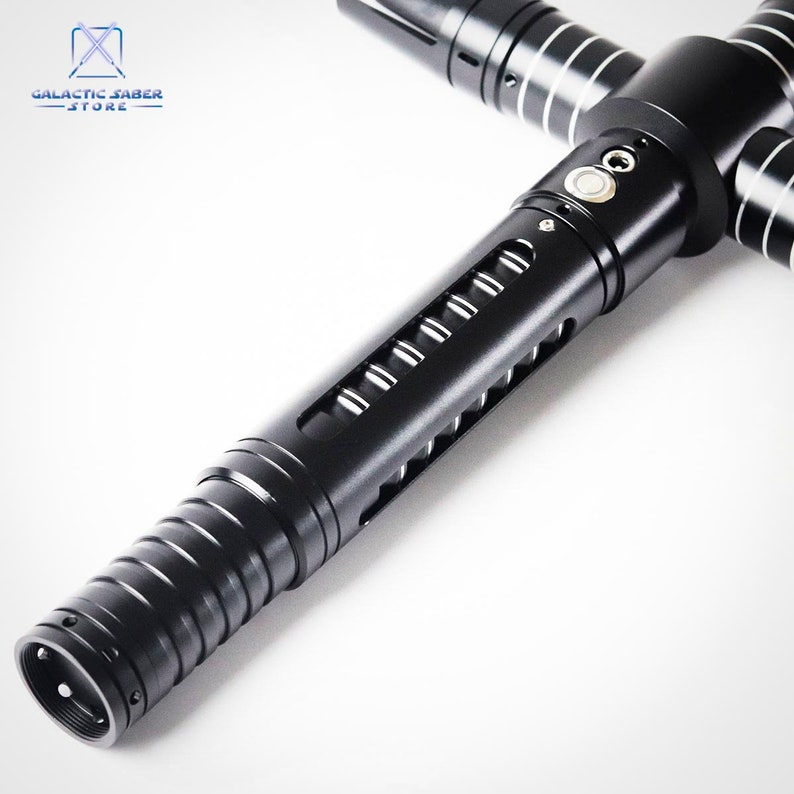 Puede incluir: Un sable de luz negro con un dise&ntilde;o de guarda cruzada. El mango presenta una serie de ranuras y un bot&oacute;n. El sable de luz tiene detalles plateados y est&aacute; sobre un fondo blanco. El logotipo de Galactic Saber Store est&aacute; en la esquina superior izquierda.