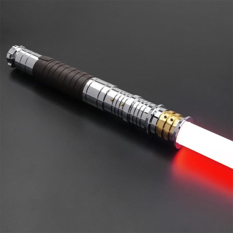 May include: A silver and brown lightsaber with a red blade. The lightsaber has a textured brown grip and a silver metal hilt with gold accents.
