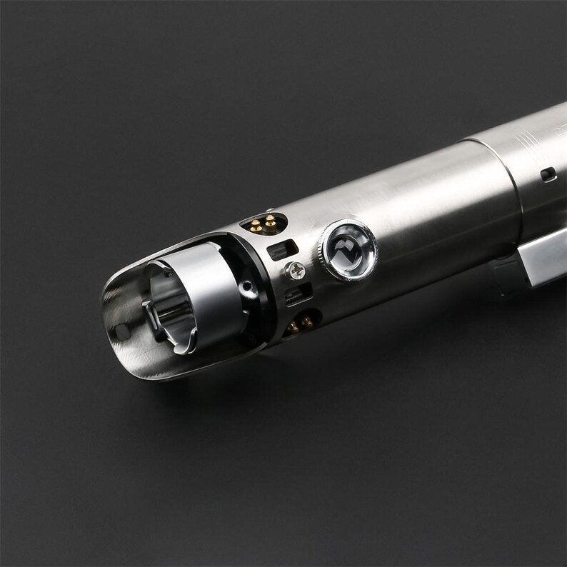 May include: A silver lightsaber hilt with a detailed design and a small, round, silver knob on the side.