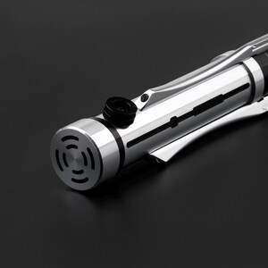 May include: A silver lightsaber with a black handle and a black and silver emitter. The lightsaber has a series of black lines running along the length of the handle.