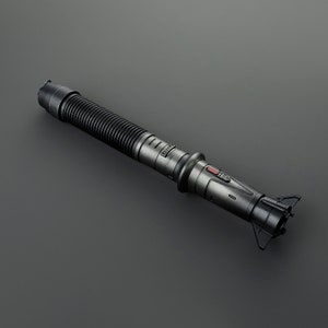 May include: A black lightsaber with a textured handle and a red button. The lightsaber has a silver tip and a black and silver handle.