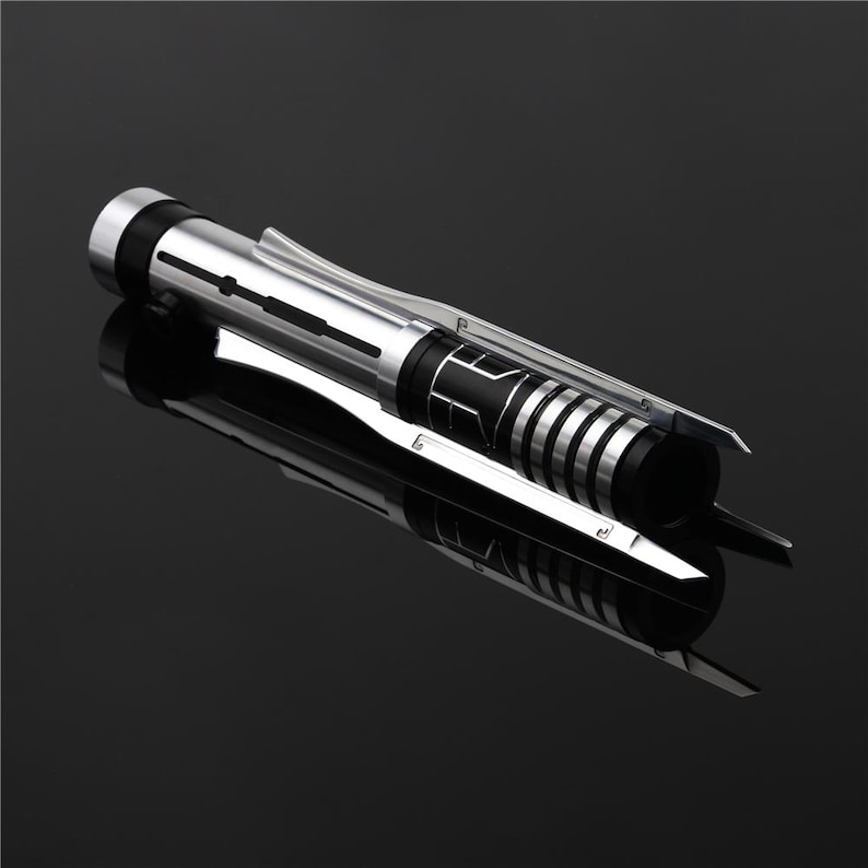May include: A silver and black lightsaber with a black handle and a silver blade. The blade is retractable and has a black grip.
