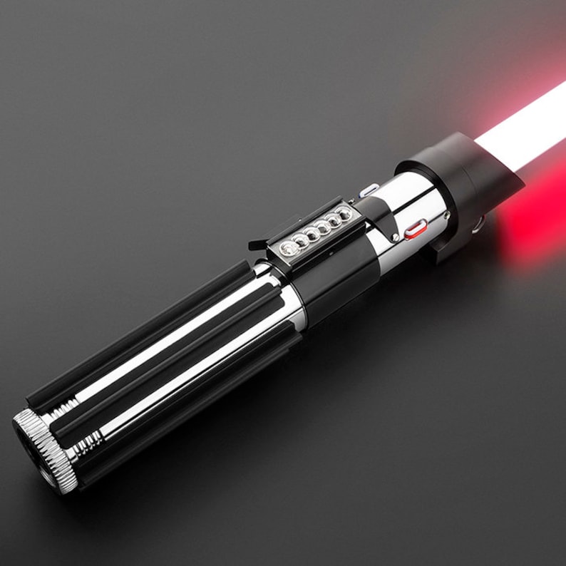 Op de afbeelding: Een zwart en zilveren lightsaber-speelgoed met een rood lichtzwaard. De lightsaber heeft een zwarte handgreep met zilveren accenten en een rode knop aan de zijkant.