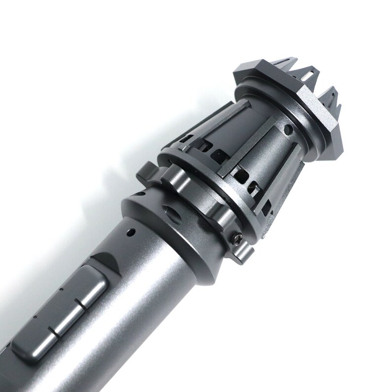 May include: A gray metal lightsaber with a textured, detailed handle and a black, pointed tip.