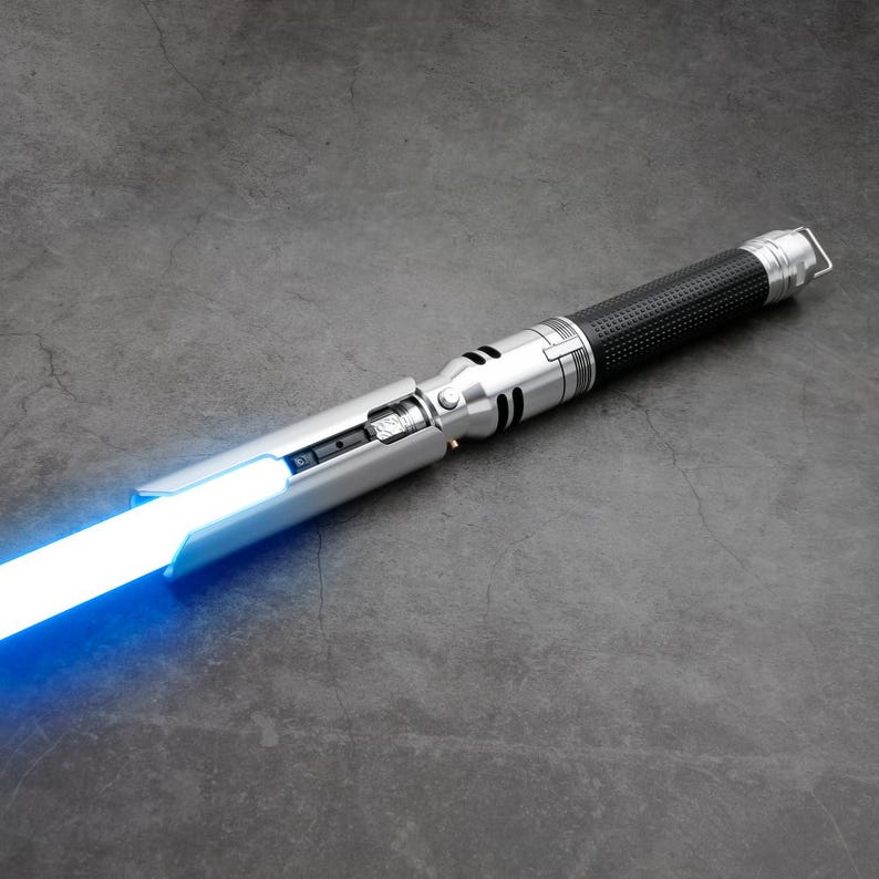 May include: A silver and black lightsaber with a blue blade. The lightsaber has a textured black handle and a silver blade holder.
