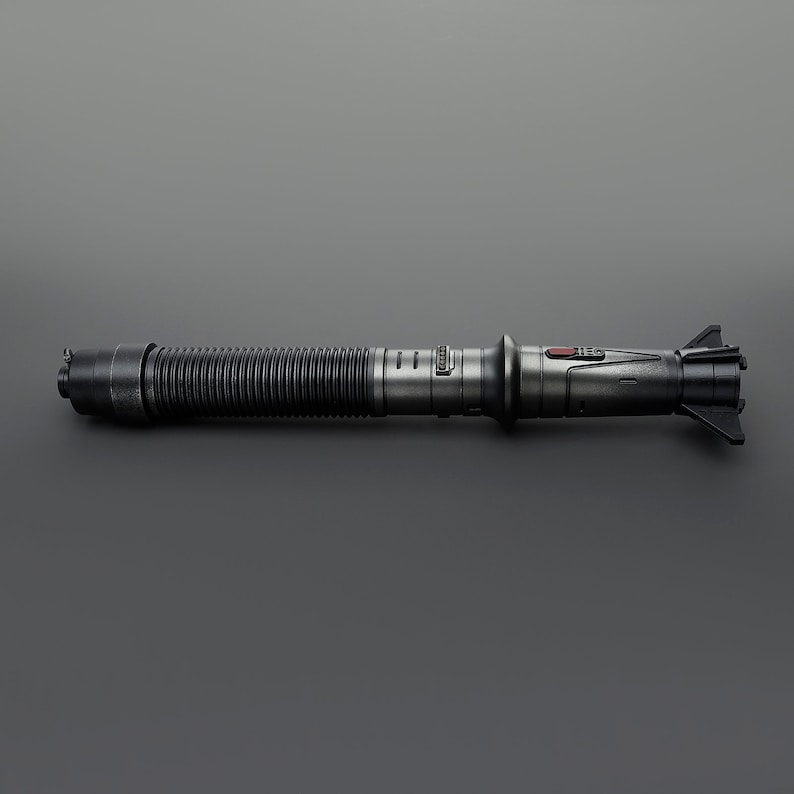 May include: A black lightsaber with a silver handle and a red button. The lightsaber has a textured, ribbed handle and a black blade.