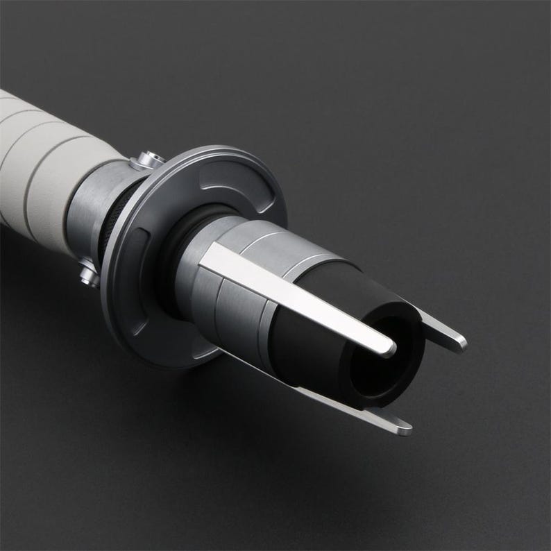 Peut inclure: Gros plan sur une poign&eacute;e de sabre laser argent&eacute;e et noire avec une poign&eacute;e blanche. La poign&eacute;e a une surface textur&eacute;e et un &eacute;metteur noir avec un anneau argent&eacute; autour.