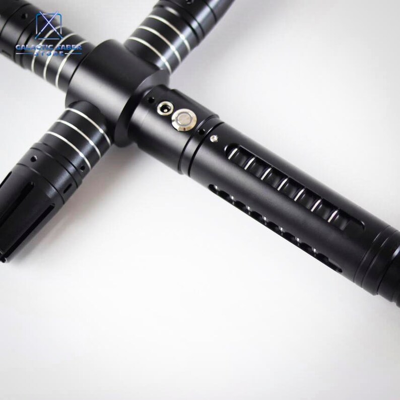 Puede incluir: Un sable de luz negro con guarda cruzada y detalles plateados. El mango tiene un bot&oacute;n y aberturas tipo ranura. El dise&ntilde;o incluye un emisor en forma de cruz. El logotipo de Galactic Saber Store es visible.