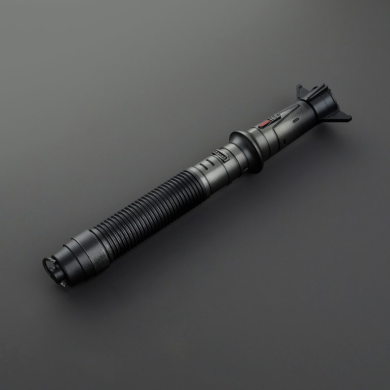 May include: A black lightsaber with a ribbed handle and a red button on the top. The lightsaber is made of metal and has a sleek, futuristic design.