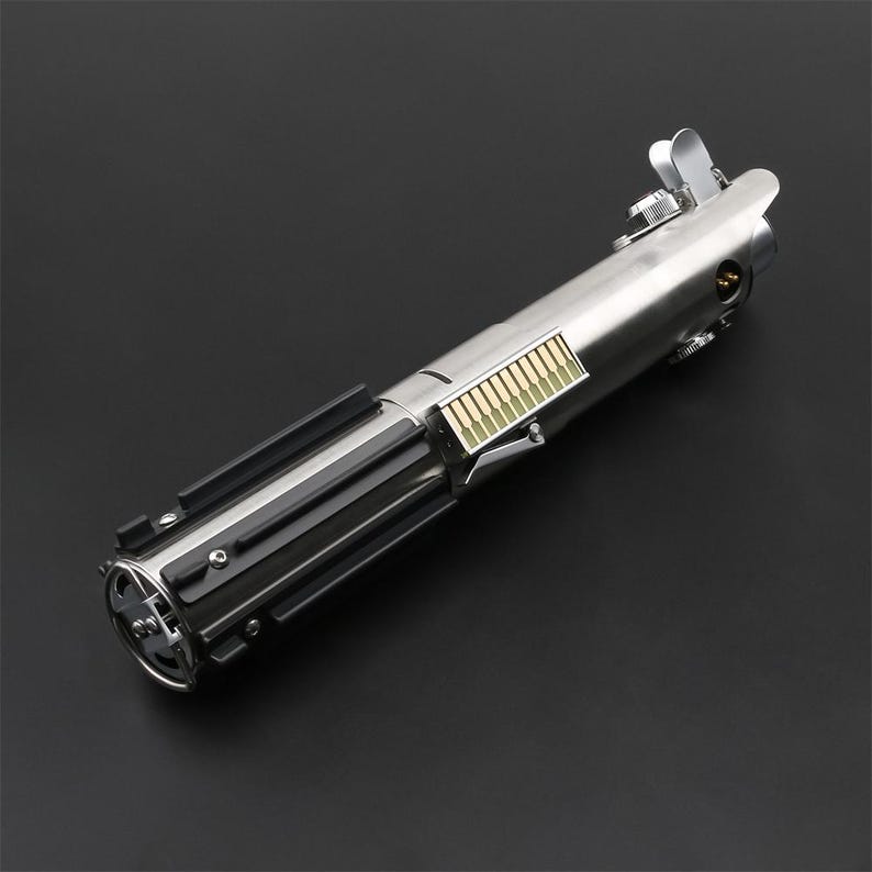 May include: A silver and black lightsaber replica with a gold-colored detail on the handle. The lightsaber is a popular collectible for fans of the Star Wars franchise.