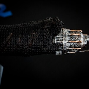May include: A detailed model of a spaceship with a weathered, metallic finish. The spaceship has a long, cylindrical body with a pointed nose and a series of small, rectangular windows. The model is partially covered in a black, textured material.