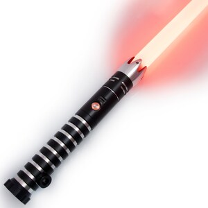 Op de afbeelding: Een zwart en zilveren lightsaber met een rode blade. De lightsaber heeft een zwarte handvat met zilveren accenten en een rode knop aan de zijkant.