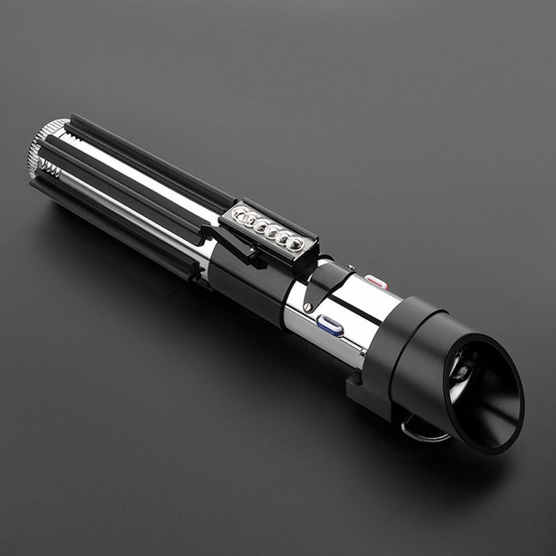 Op de afbeelding: Een zwart en zilveren lightsaber-speelgoed met een zwarte handgreep en een zilveren blad. De lightsaber heeft een knop op de handgreep en een rood licht aan het einde van het blad.