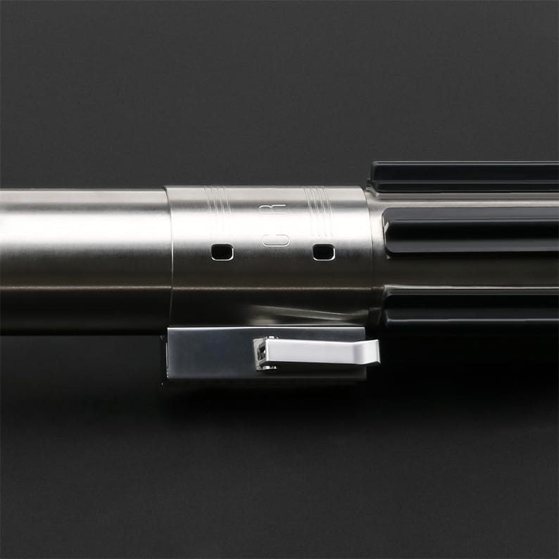 May include: A silver lightsaber hilt with a black handle and a silver switch. The hilt has a series of grooves and a small, circular opening on the side.