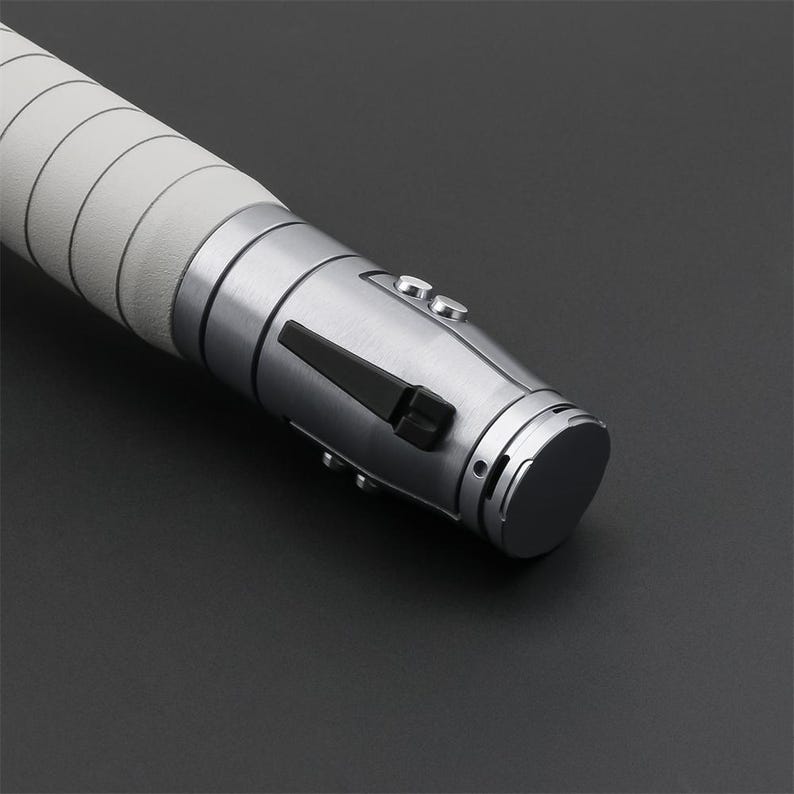 Peut inclure: Gros plan sur une poign&eacute;e de sabre laser argent&eacute;e avec un interrupteur noir et une poign&eacute;e blanche.