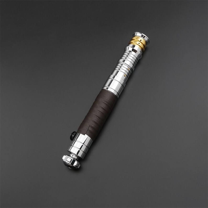 May include: A silver and brown lightsaber with a leather grip. The lightsaber has a gold accent at the top.