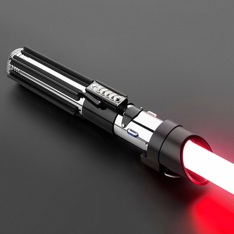 Op de afbeelding: Een zwart en zilveren lightsaber met een rode blade. De lightsaber heeft een zwarte handvat met een zilveren metalen gedeelte en een rode knop.