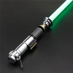 May include: A silver lightsaber with a green blade. The lightsaber has a black and silver handle with a gold accent.