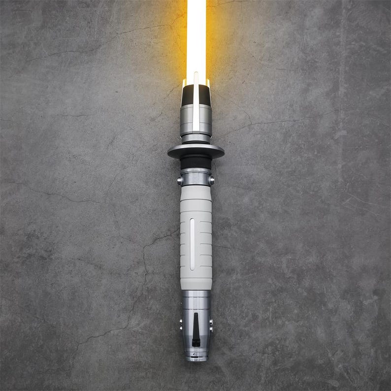 Peut inclure: Un sabre laser argent&eacute; avec une lame blanche, allum&eacute; et brillant sur un fond gris.