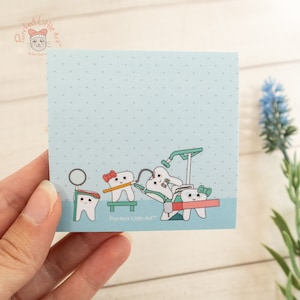 May include: A blue card with white polka dots features a cartoon illustration of five teeth. The teeth are wearing hats, bows, and glasses. The teeth are holding dental tools and are in a dentist's chair. The text "Purrfect Little Art™" is at the bottom of the card.