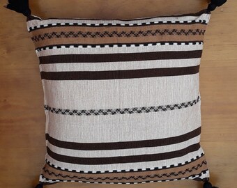 May include: A decorative throw pillow with a brown, white, and beige striped pattern. The pillow has tassels on each corner.