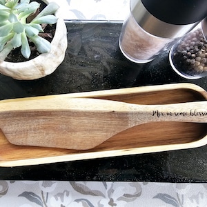 May include: A wooden serving dish with a wooden spatula. The spatula has the words "Mix in some blessings" engraved on it.