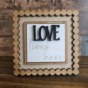 May include: A wooden sign with a scalloped frame and the words "LOVE lives here" in black lettering.