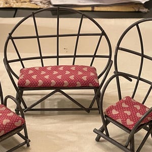 May include: Three metal chairs with pink heart patterned cushions. The chairs are made of a thin metal frame and have a simple design.