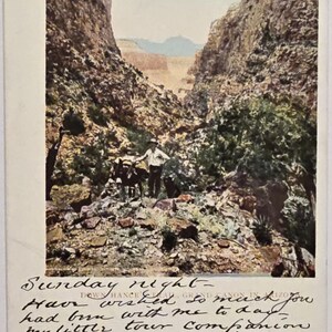 May include: A vintage postcard showing a canyon landscape with a man and pack animals. The colour photograph has handwritten text at the bottom, possibly a personal message. The canyon walls are rugged, and the sky is a pale blue.