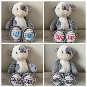 May include: Four plush cow toys with personalized names on their feet. The cows are white with black spots and have gray fur. The names on the feet are: Kira Jennings, Charli Ray, Hallie Faye, and Ambrose Cupertino.