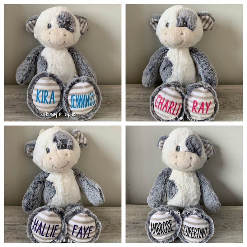 May include: Four plush cow toys with personalized names on their feet. The cows are white with black spots and have gray fur. The names on the feet are: Kira Jennings, Charli Ray, Hallie Faye, and Ambrose Cupertino.