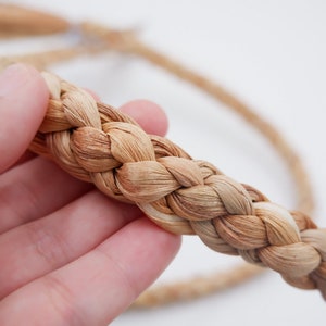 May include: A close-up of a braided rope made from natural fibers. The rope is light brown in color and has a rough texture. It is braided in a traditional style, with the strands of fiber interwoven to create a strong and durable cord.