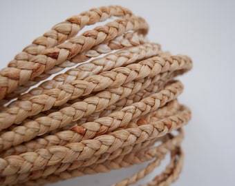 May include: Close-up of a braided rope made of natural fibers. The rope is light brown in color and has a slightly rough texture. The rope is braided in a tight pattern, creating a strong and durable cord.