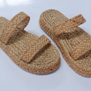 May include: A pair of woven straw sandals with two straps. The sandals are light brown in color and have a flat sole.