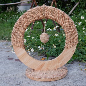 May include: A wooden cat toy with a circular base and a ring of woven rope. A dangling ball of woven rope hangs from the ring.