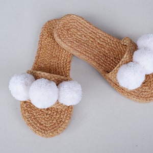 May include: A pair of woven straw slippers with white pom-poms.
