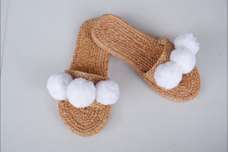 May include: A pair of woven straw slippers with white pom-poms.