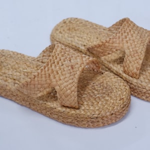 May include: A pair of woven straw sandals with a criss-cross strap design. The sandals are light brown in color and have a flat sole.