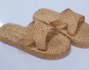 May include: A pair of woven straw sandals with a criss-cross strap design. The sandals are light brown in color and have a flat sole.