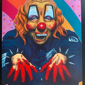 May include: A creepy clown with a red nose and a wide smile is wearing a blue jacket with a black patch on the sleeve. The clown has spiky bracelets on both wrists and bloody hands. The background is a rainbow with pink stars.