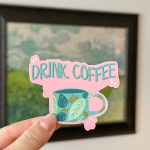 May include: Pink sticker with the text "DRINK COFFEE" in teal lettering. A teal coffee mug with a leafy pattern is below the text.