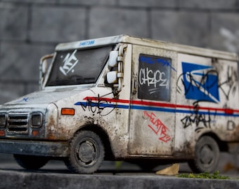 May include: A white USPS mail truck with graffiti and a blue and red stripe. The truck has a license plate that reads "5467366".