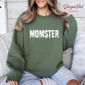 A woman wearing a green sweatshirt with the word "MOMSTER" printed on it.