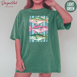 A person wearing a green t-shirt with a graphic design of three colorful fish swimming in a row.
